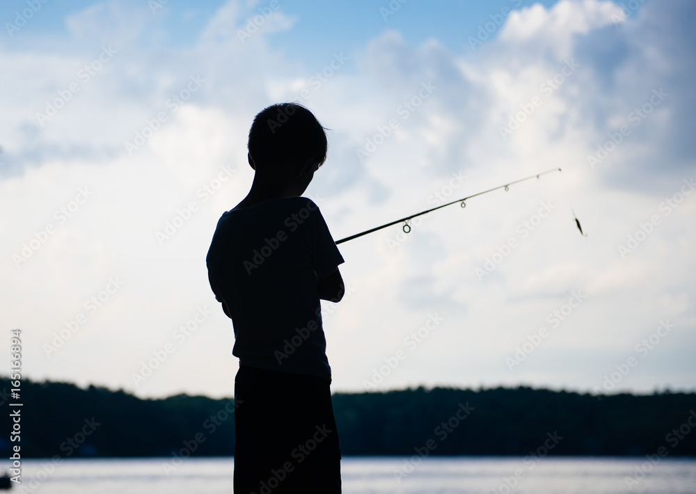 Silhouette of a boy fishing on a lake at sunset Stock Photo