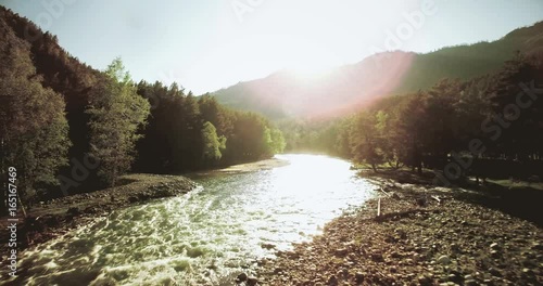 4k (UHD) aerial view. Low flight over fresh cold mountain river at sunny summer morning. Green trees and sun rays.