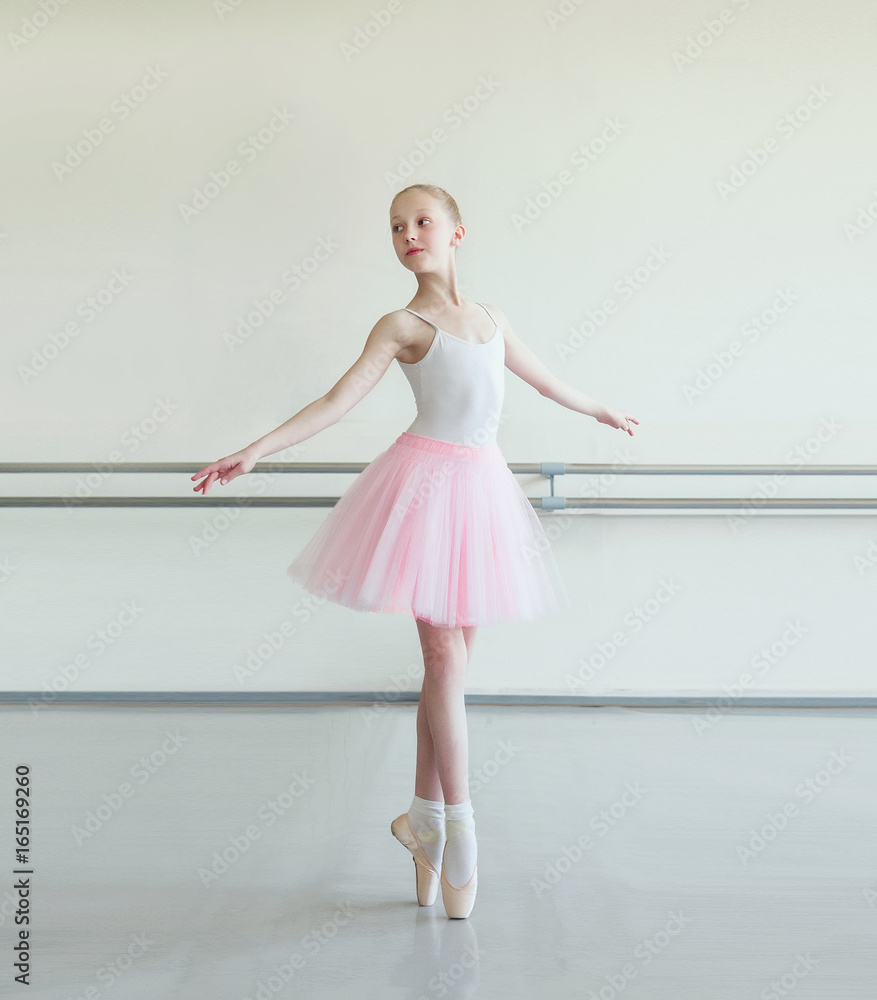 Cute little ballerina in pink ballet costume and pointe shoes is dancing in  the room. Kid in dance class. Child girl is studying ballet. Copy space.  Stock Photo