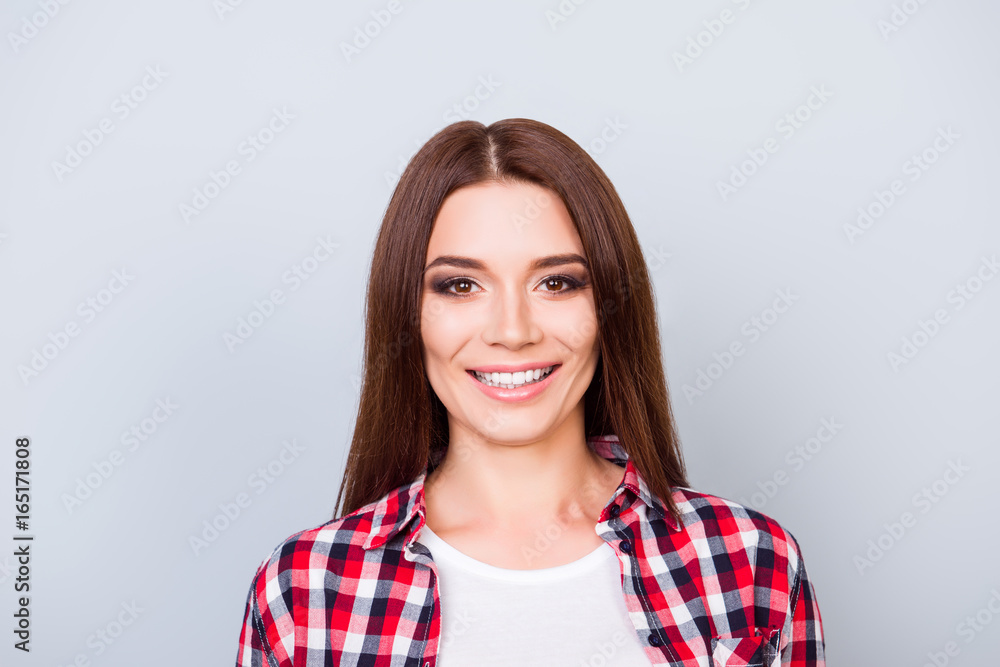 Young gorgeous brunette girl is standing on the pure light blue background and smiling, wearing casual checkered shirt, with beaming smile Young gorgeous brunette girl is standing on the pure light blue background and smiling, wearing casual checkered shirt, with beaming smile