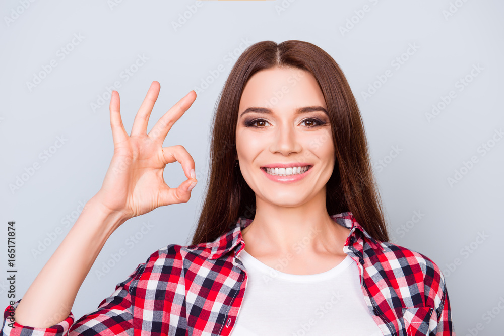 Cheerful young brunette pretty girl on the pure blue background is smiling, wearing casual checkered shirt and showing ok sign, looking charming and feminine Cheerful young brunette pretty girl on the pure blue background is smiling, wearing casual checkered shirt and showing ok sign, looking charming and feminine