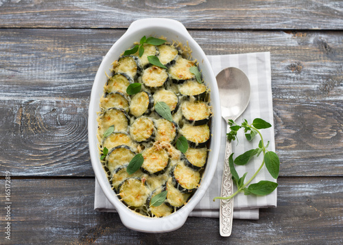 Gratin zucchini with cheese and greens on a wooden background. Delicious homemade food