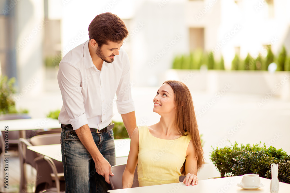 True gentleman! Young handsome brunet lover is adjusting the chair of his happy lady, both well dressed, at a sunny terrace of restaurant True gentleman! Young handsome brunet lover is adjusting the chair of his happy lady, both well dressed, at a sunny terrace of restaurant