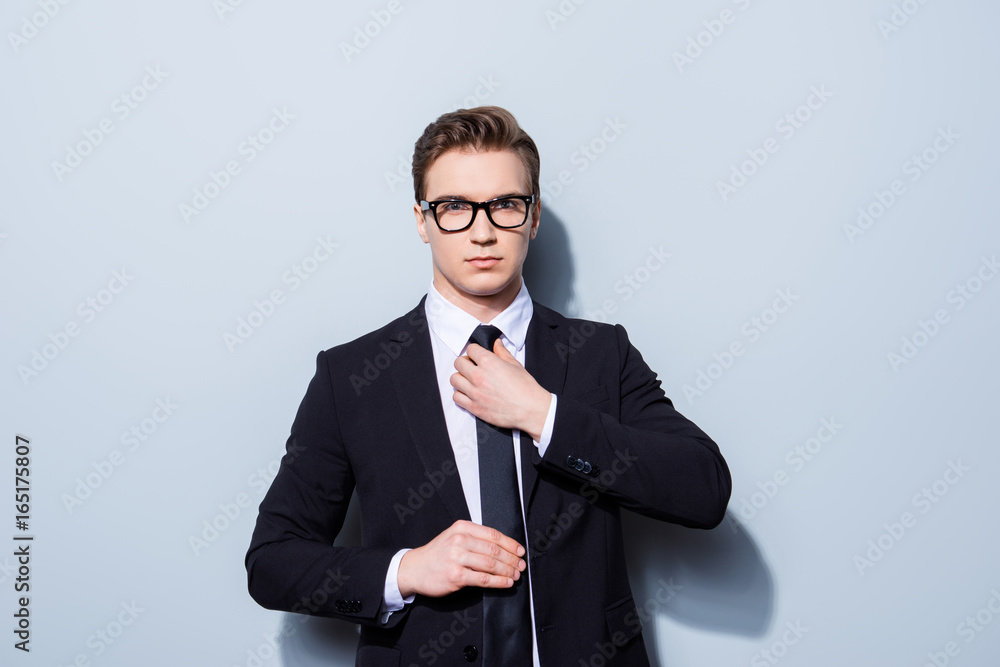 Young attractive businessman banker is standing on the pure light background. He looks stunning! So severe and confident, in tuxedo and glasses