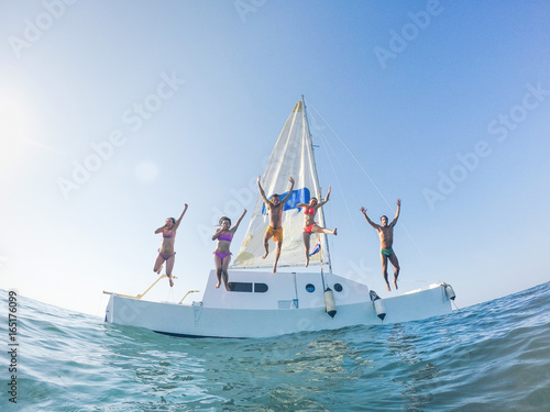 Happy friends jumping off the catamaran boat into the ocean - Young people having fun diving into the sea - Travel, tropical, summer and concept - Soft focus on center guys - Fisheye lens distorsion © DisobeyArt