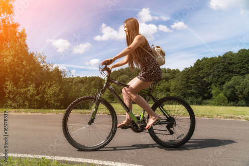 Girl riding a bicycle. Side view. Forest and clouds and a rainbow in the background