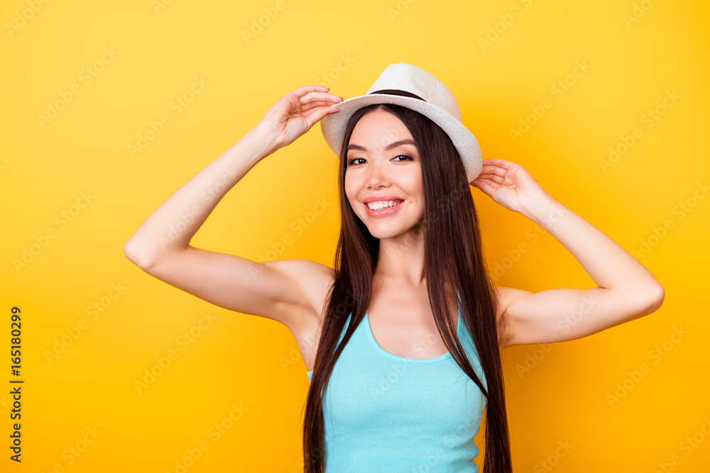 Happy young asian girl on summer vacation. She is in a stylish hat, wearing casual singlet, holding her white cap, amazed, on bright yellow background Happy young asian girl on summer vacation. She is in a stylish hat, wearing casual singlet, holding her white cap, amazed, on bright yellow background