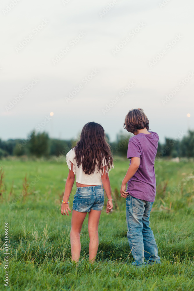 Backside of a boy and a girl standing in a grass field talking to each other Backside of a boy and a girl standing in a grass field talking to each other