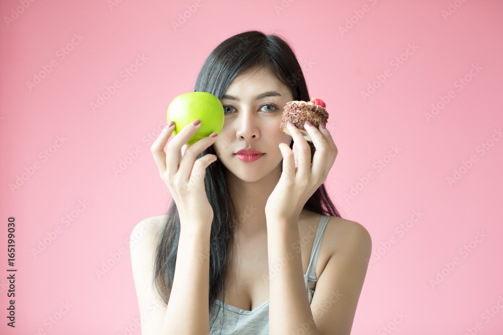 Beautiful young woman making a choice between a cake and apple Beautiful young woman making a choice between a cake and apple