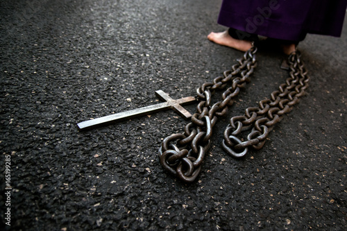 A barefoot penitent drags chains and a cross tied to his ankles during the procession of Good Friday in the streets of Madrid photo