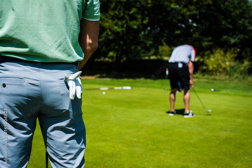 Obraz premium Golfer standing on the putting green with his gloves in his pocket, watching another