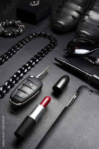Woman accessories in business style, red lipstick, gadgets, jewelry, car key, sunglasses, shoes, and other luxury businesswoman attributes on leather black background, fashion industry