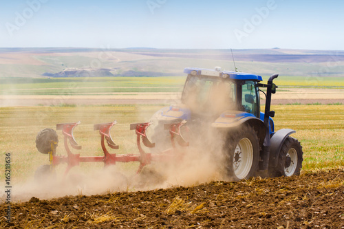 Fotografia tractor ploughing a field with trail of dust