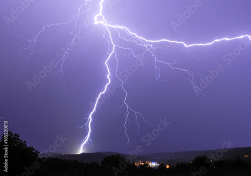 Close lightning strike on a hill and power flash over a small town