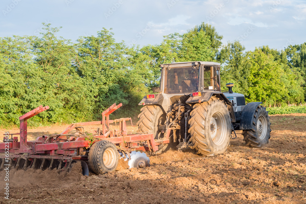 Big silver tractor with a red harrow (disc cultivator) in the field on a sunny day. The concept of work in a fields and agriculture industry. Big silver tractor with a red harrow (disc cultivator) in the field on a sunny day. The concept of work in a fields and agriculture industry.