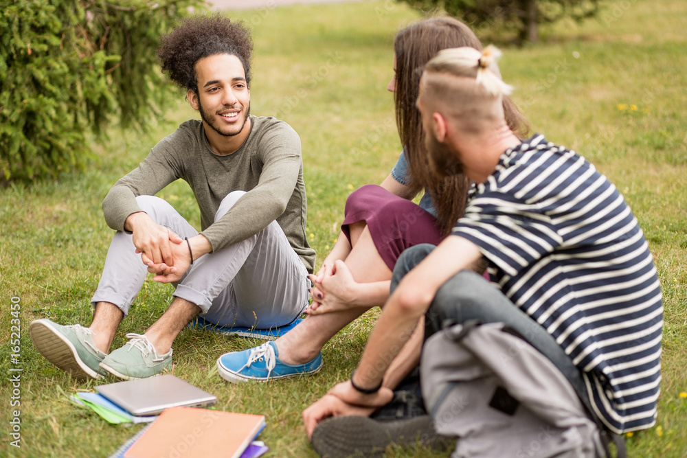 Students sitting at lawn talking after classes. Young men and girl relaxing at grass. Students sitting at lawn talking after classes. Young men and girl relaxing at grass.