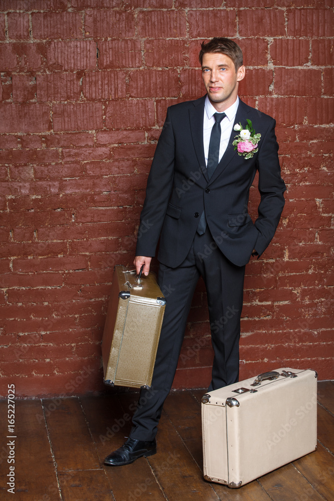 Fototapeta premium groom is a brick wall with two suitcases