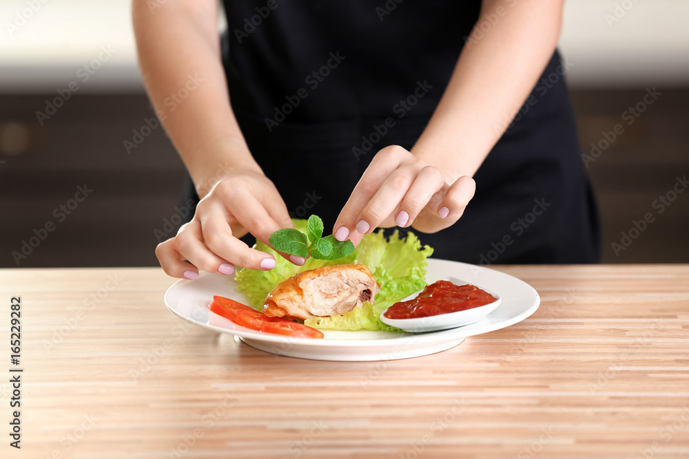 Female hands adding mint leaves to yummy fried chicken thigh with sauce on white plate Female hands adding mint leaves to yummy fried chicken thigh with sauce on white plate