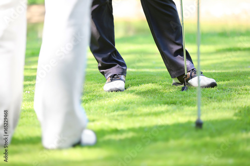 Legs of young men playing golf on course in sunny day