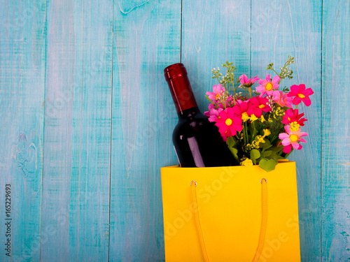 bottle of wine and flowers in the package on wooden background, space for text