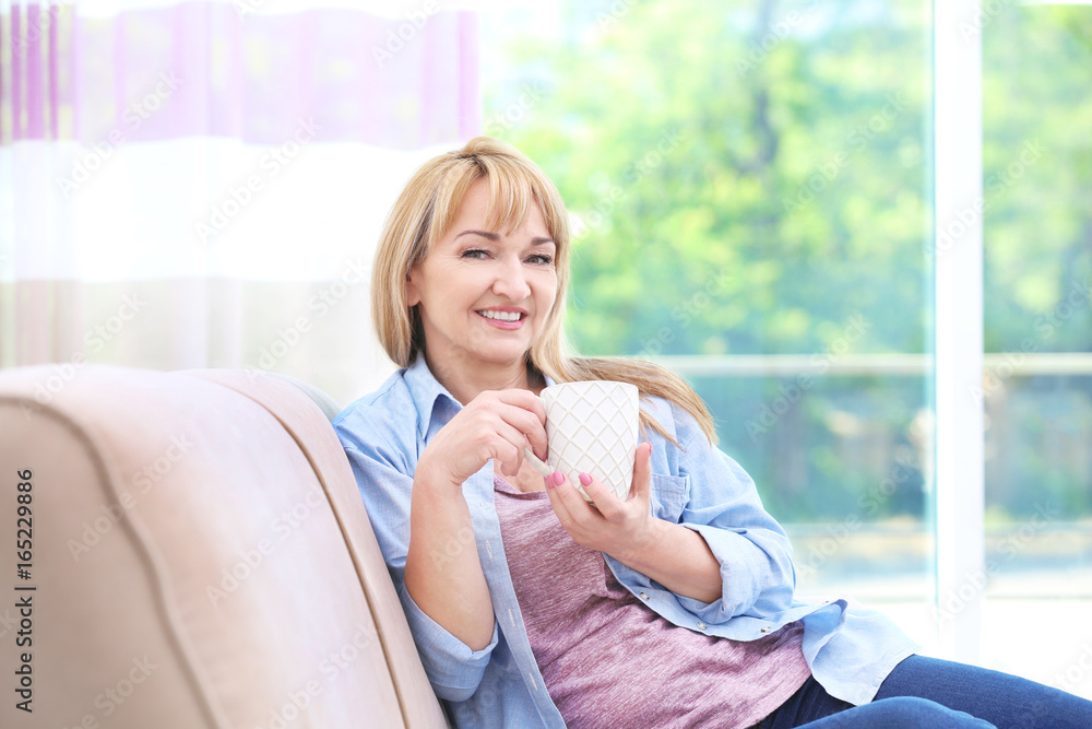 Attractive smiling mature woman sitting on sofa at home Attractive smiling mature woman sitting on sofa at home