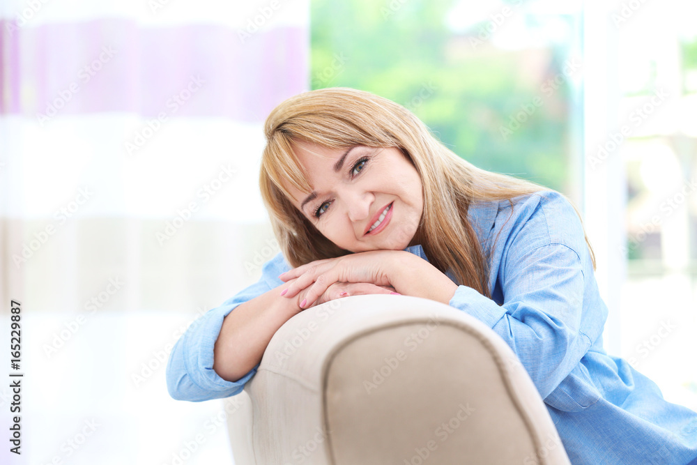 Attractive smiling mature woman sitting on sofa at home Attractive smiling mature woman sitting on sofa at home