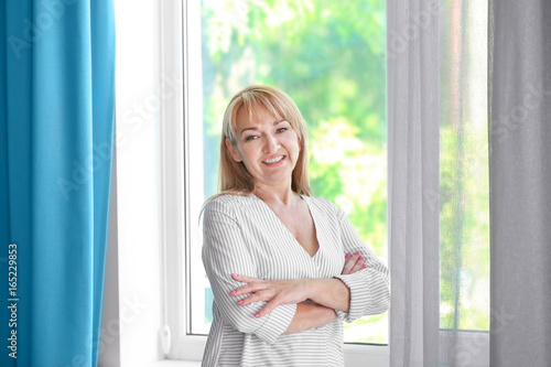 Attractive mature woman standing near window