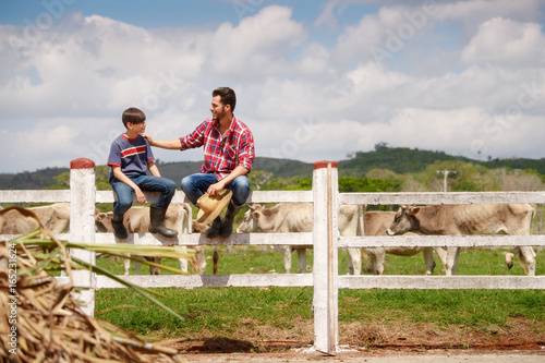 Happy Father And Son Smiling In Farm With Cows