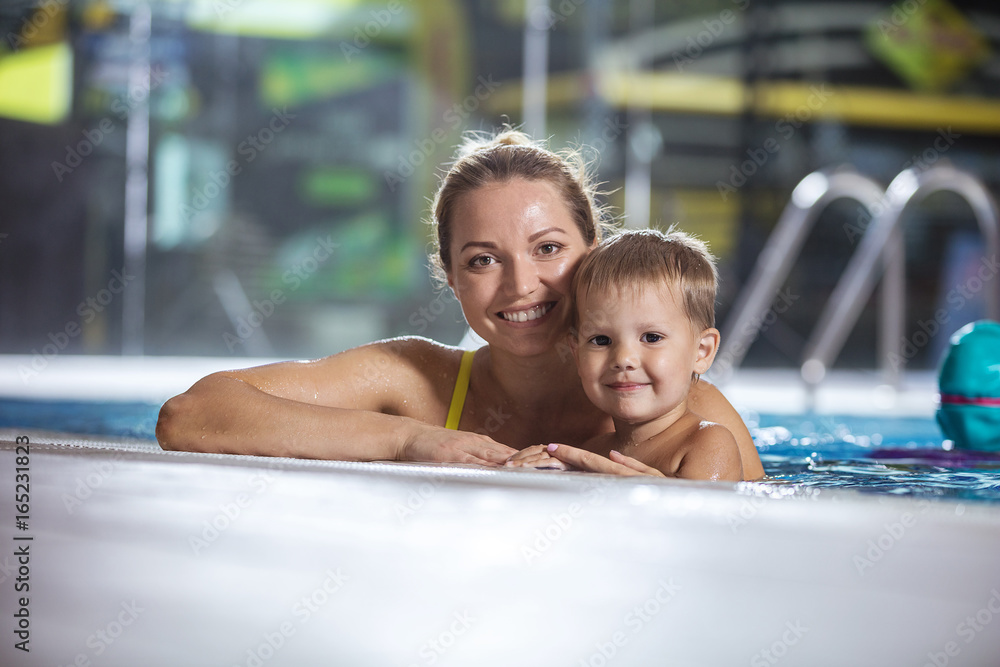 Happy young woman with little son smiling in indoor pool