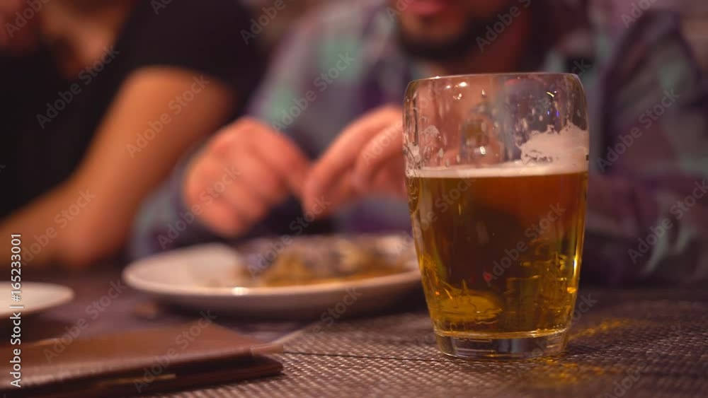 A young man is drinking beer in a bar with dluzyami. Close-up of light beer with foam. In the background, the guy has capelin. Fried appetizing fish in hands.The hand stretches the menu with the score A young man is drinking beer in a bar with dluzyami. Close-up of light beer with foam. In the background, the guy has capelin. Fried appetizing fish in hands.The hand stretches the menu with the score