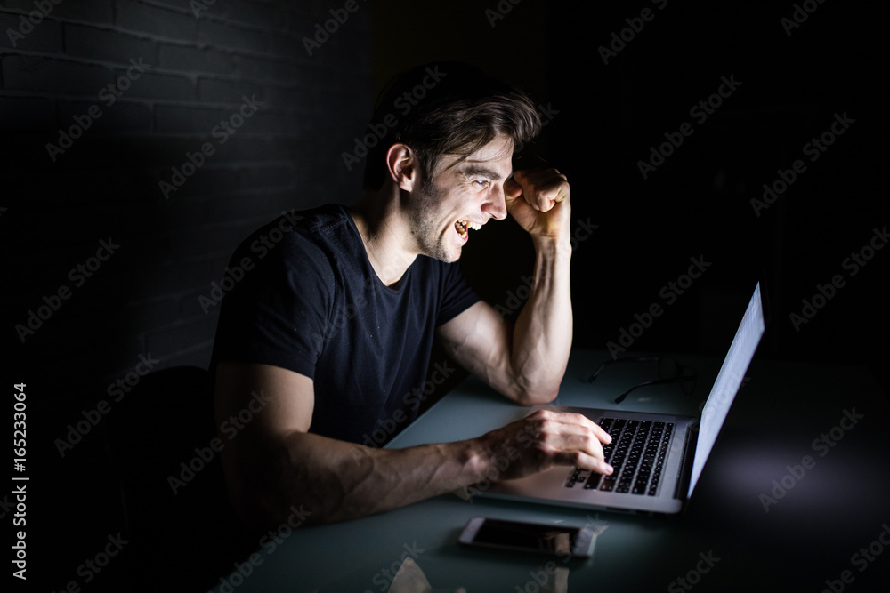 Young man working on computer at night in dark office the designer works in the later time Young man working on computer at night in dark office the designer works in the later time