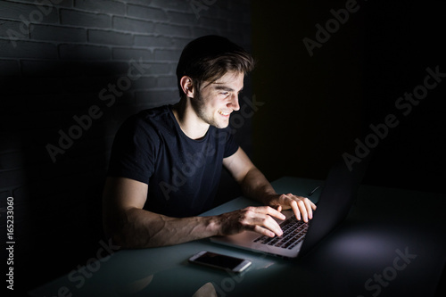 Young man using laptop to stay all night in social nerworks at home table