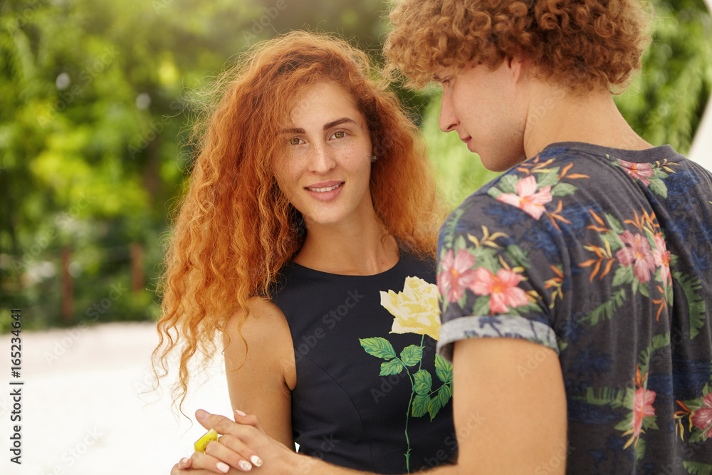 Portrait of lovely red-haired woman with beautiful appearance spending her  free time with boyfriend dancing at green park having fun together. Young  guy looking at her redhead girlfriend with love Stock Photo |