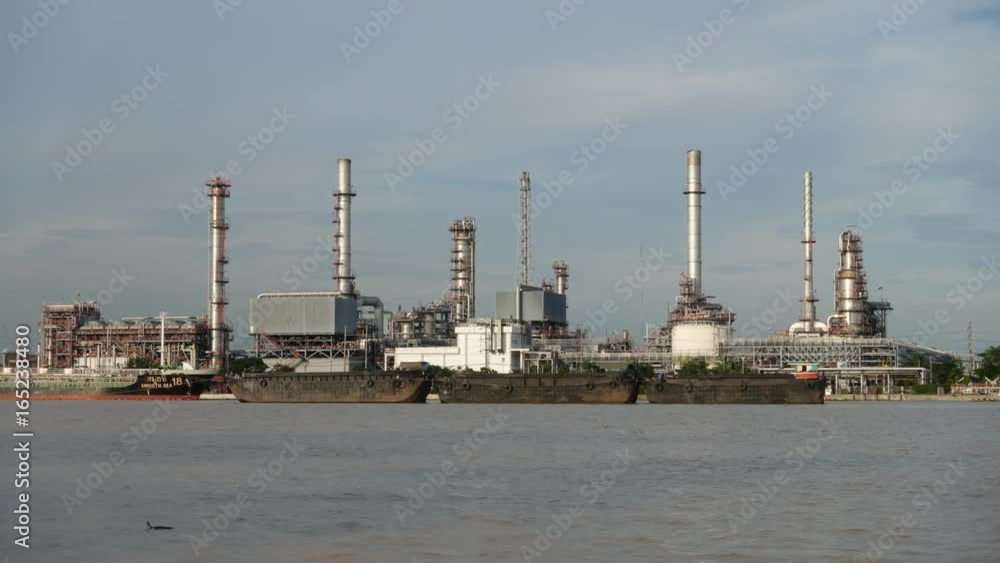 Time lapse. Cargo container ship, Carrier boat floating and moving in river with Oil Petrochemical energy plant background. Business Industry and Logistics shipping, maritime transportation concept Time lapse. Cargo container ship, Carrier boat floating and moving in river with Oil Petrochemical energy plant background. Business Industry and Logistics shipping, maritime transportation concept