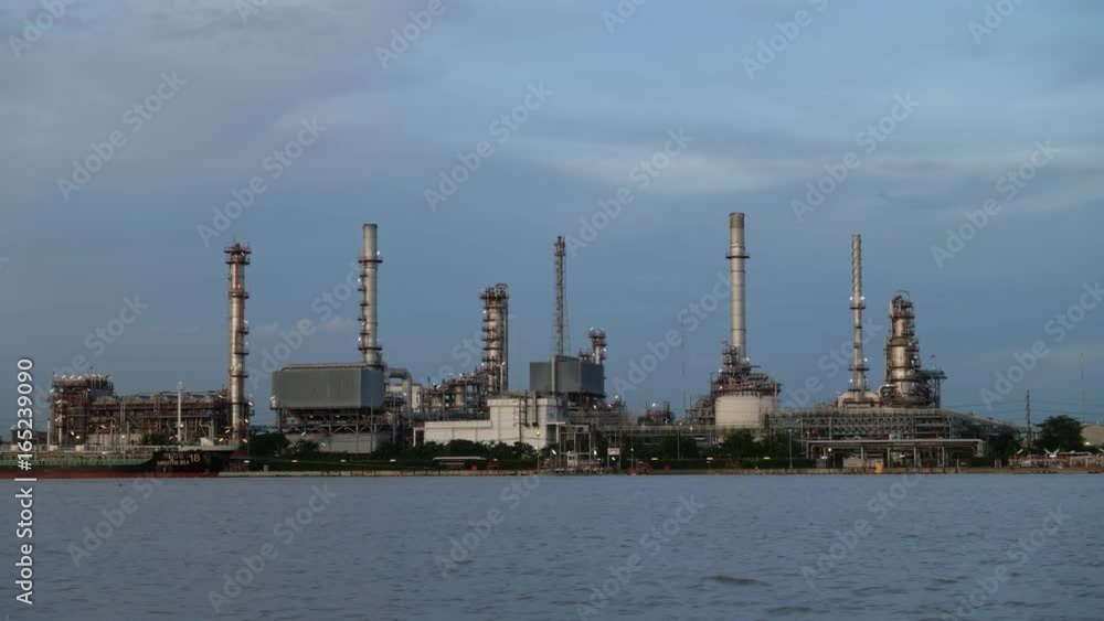 Time lapse. Cargo container ship, Carrier boat floating and moving in river with Oil Petrochemical energy plant background. Business Industry and Logistics shipping, maritime transportation concept Time lapse. Cargo container ship, Carrier boat floating and moving in river with Oil Petrochemical energy plant background. Business Industry and Logistics shipping, maritime transportation concept
