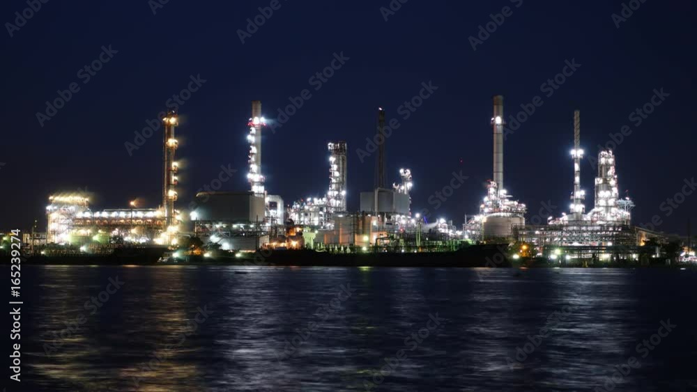 Time lapse. Cargo container ship, Carrier boat floating and moving in river with Oil Petrochemical energy plant background. Business Industry and Logistics shipping, maritime transportation concept Time lapse. Cargo container ship, Carrier boat floating and moving in river with Oil Petrochemical energy plant background. Business Industry and Logistics shipping, maritime transportation concept