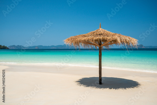 Beach Umbrella made of leafs on white beach in front of Sea day time blue sky wide shot background © happystock