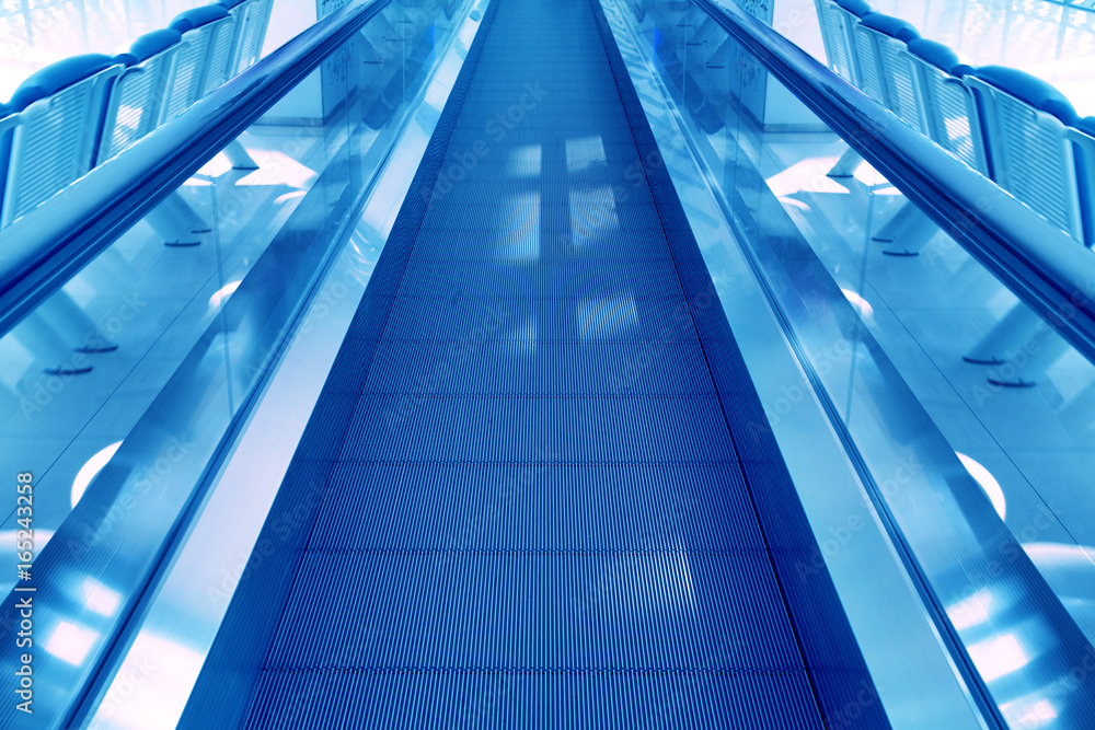 Travel concept. Escalator walk way inside modern airport terminal. Image in blue colors Travel concept. Escalator walk way inside modern airport terminal. Image in blue colors