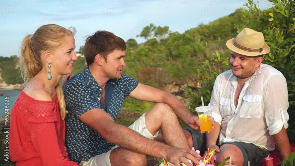 Friends on picnic on Bali cliff shore sitting and talking Friends on picnic on Bali cliff shore sitting and talking