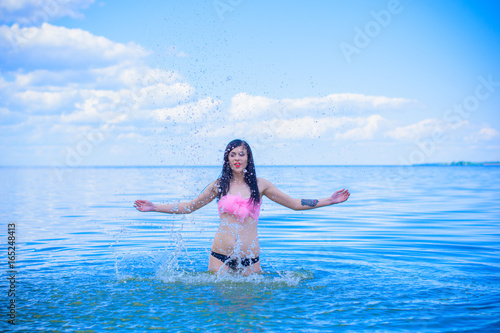 A wet beautiful sexy young woman bathes in the blue water, showing off her beauty. The concept of female beauty, sports figure and healthy lifestyle