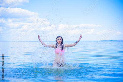 A wet beautiful sexy young woman bathes in the blue water, showing off her beauty. The concept of female beauty, sports figure and healthy lifestyle photo