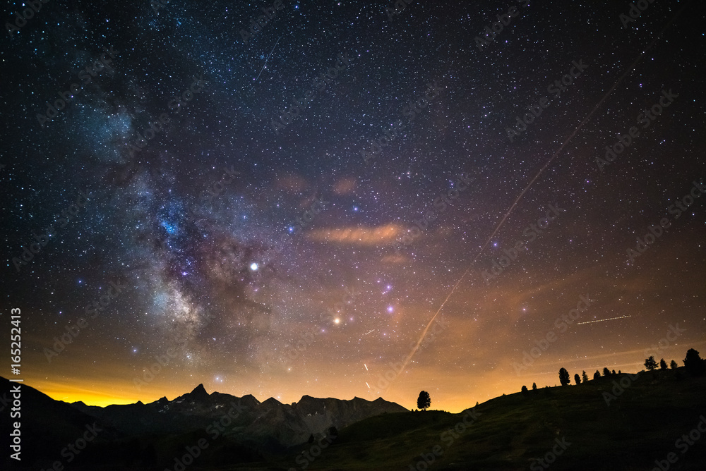Fototapeta premium The colorful glowing core of the Milky Way and the starry sky captured at high altitude in summertime on the Italian Alps, Torino Province. Airplane traffic in the sky.
