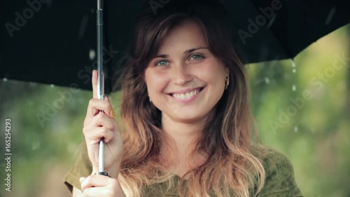 Beautiful woman is standing under the umbrella during the rain and sincerely laughing, enjoying nature