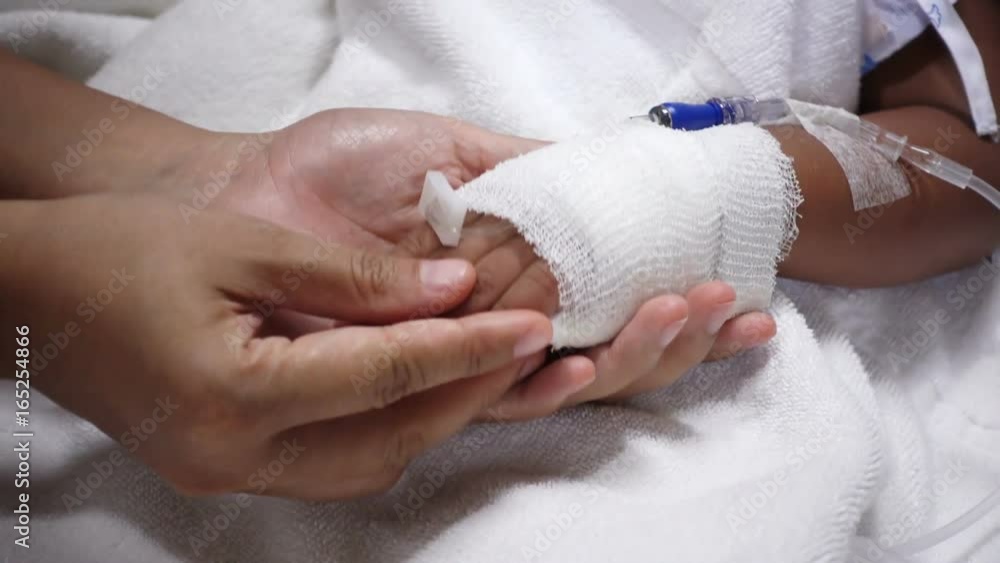 Close up of young parent and sick little daughter holding bandaged hands for comfort in a hospital bed Close up of young parent and sick little daughter holding bandaged hands for comfort in a hospital bed