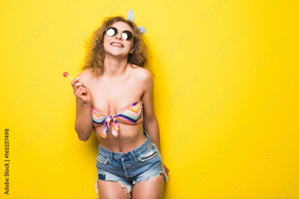 Happy modern woman smiling with a lollipop candy over yellow background Happy modern woman smiling with a lollipop candy over yellow background