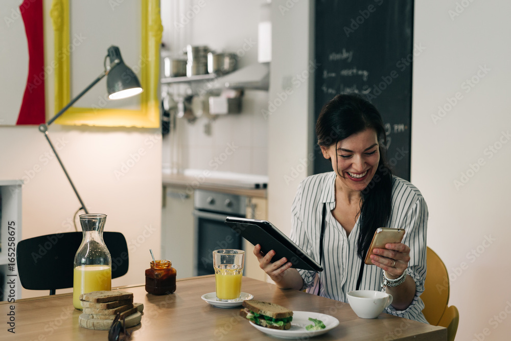 Social media time.young woman having breakfast while using her tablet and mobile phone at her home Social media time.young woman having breakfast while using her tablet and mobile phone at her home