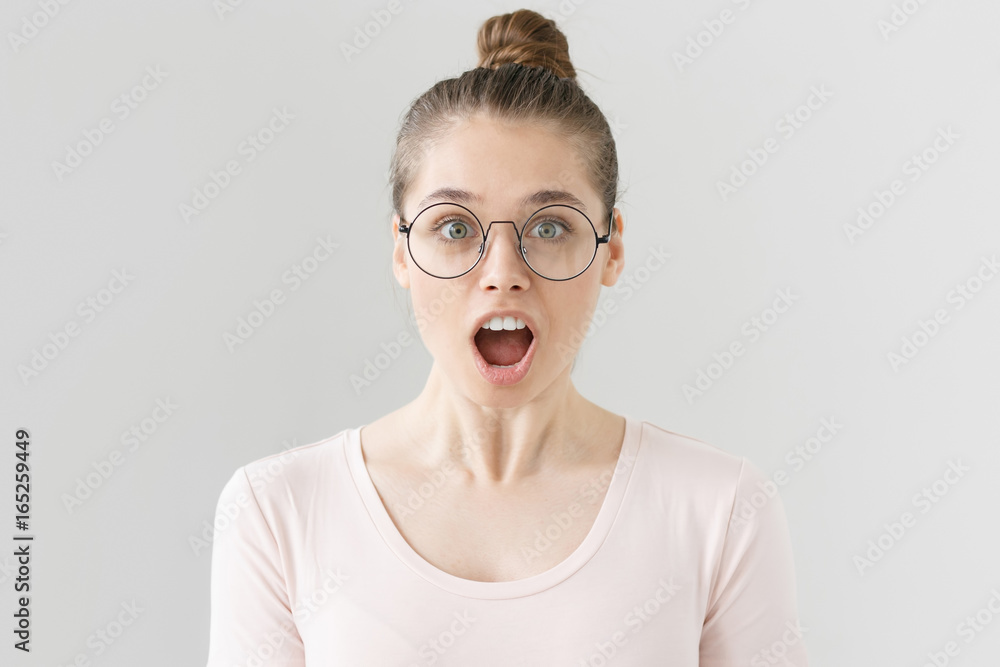 Closeup portrait of young beautiful woman isolated on gray background, wearing big round spectacles, opening her mouth wide in astonishment, surprised with unbelievable news or commercial offer. Closeup portrait of young beautiful woman isolated on gray background, wearing big round spectacles, opening her mouth wide in astonishment, surprised with unbelievable news or commercial offer.