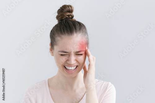 Beautiful young woman squeezing face because of strong pain  putting one hand to head  screaming and curving mouth in suffering from migraine
