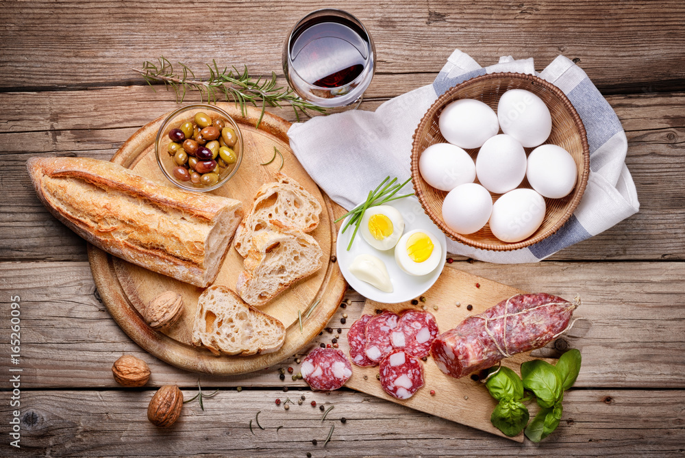 Salami, eggs, bread, olive and red wine on a wooden background