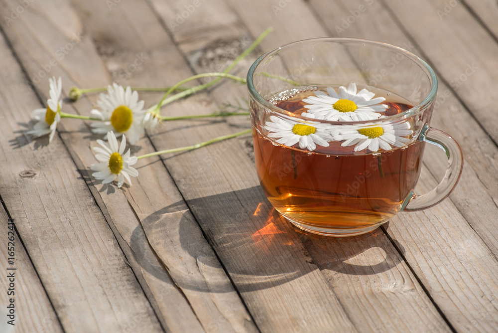 Herbal tea with chamomile on a wooden table on a summer sunny morning Herbal tea with chamomile on a wooden table on a summer sunny morning